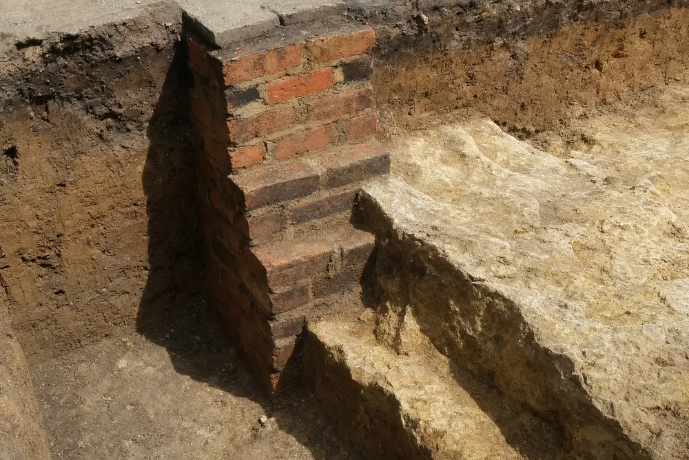 A trench in which a brick footing steps down onto a pale rock ledge — underpinning, Sydney. Illustrative example.